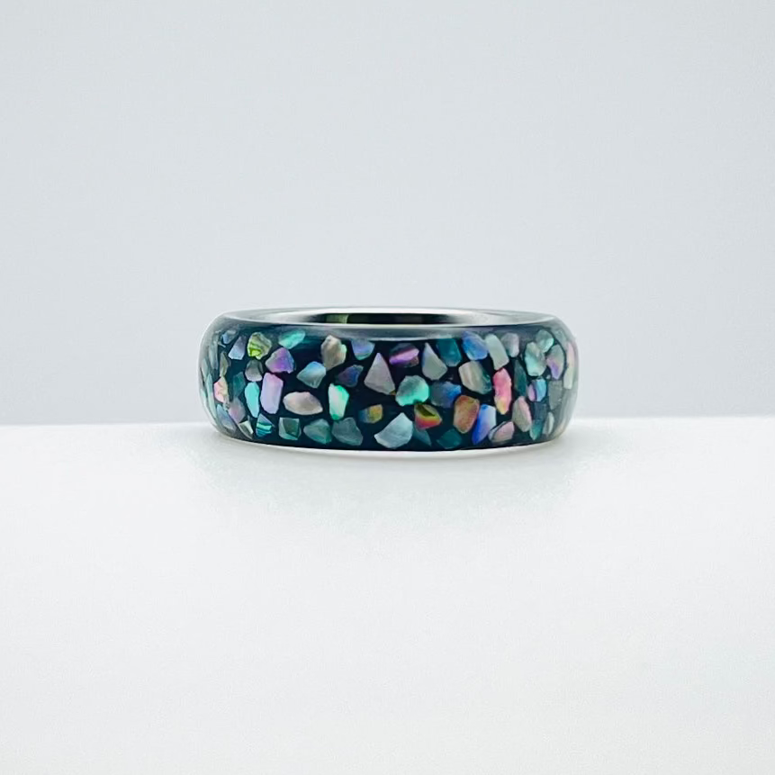 Tungsten ring with multi-color abalone shell pieces on a white background