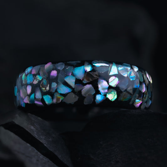 Tungsten ring with multi colored abalone shell pieces on a dark stone background