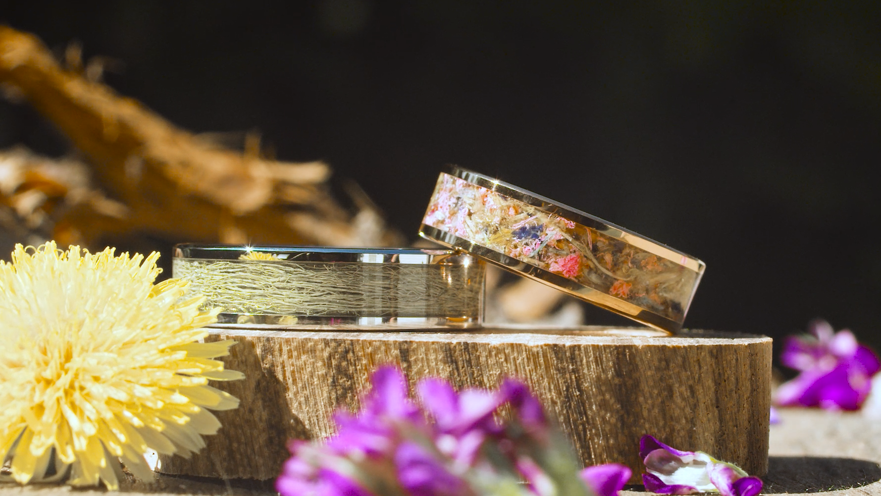 Two rings with floral designs on a wooden block with flowers around them
