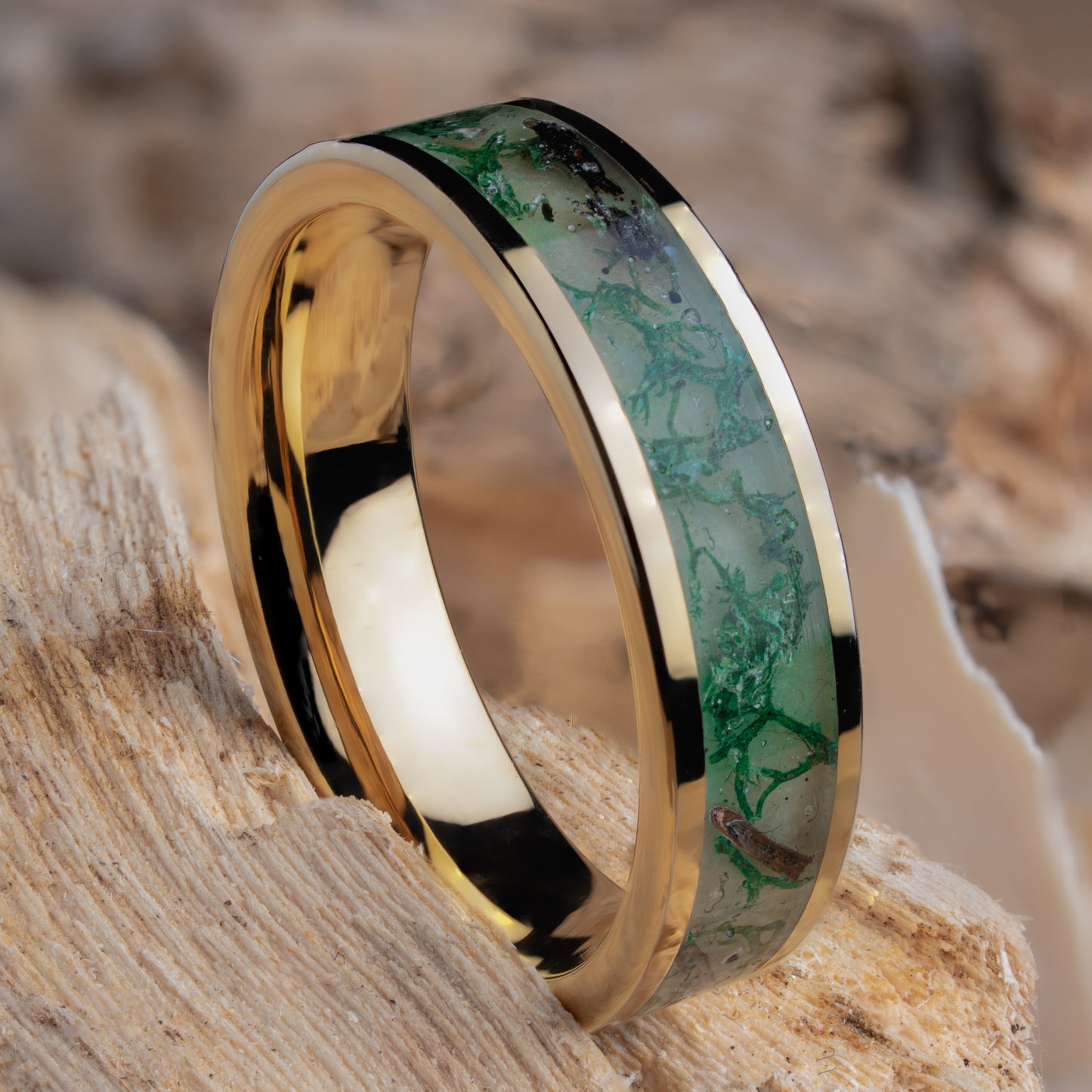 Gold plated tungsten ring with green glow powder, dried moss, and twigs inside on a natural wooden background