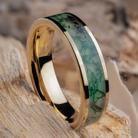 Gold plated tungsten ring with green glow powder, dried moss, and twigs inside on a natural wooden background