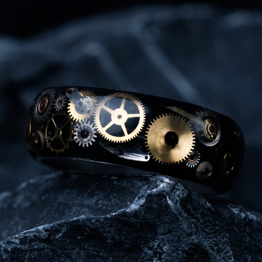 Tungsten ring with antique gold and silver watch parts inside sitting on a dark rock