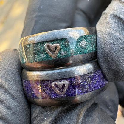 Two carbon fiber rings made with purple and teal pigment powders, meteorite shavings, and small metal hearts from engagement rings inside